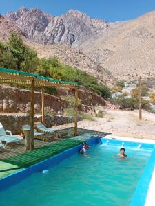 two people swimming in a swimming pool with mountains in the background at Hermosa casa familiar para 8 personas - Cochiguaz Valle de Elqui in Paihuano