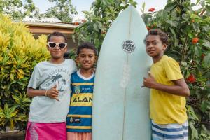 three young boys are standing next to a surfboard at Sujees surf stay, cloudbreak in Nadi