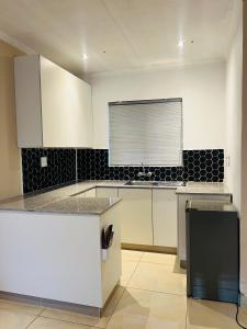 Emgwenyeni Guest house في منزيني: مطبخ مع خزائن بيضاء وجدار بلاط أسود