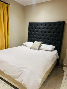 Emgwenyeni Guest house في منزيني: غرفة نوم بسرير كبير مع لوح أمامي أسود +3 صور