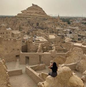 una donna seduta su una roccia che guarda verso una città di Shali Castle Apartment a Siwa