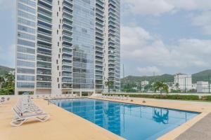 a swimming pool with lounge chairs and a tall building at Amazing Condo Ocean View By Bamboo Skylife in Acapulco
