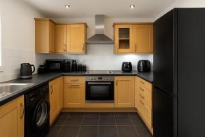 Stylish 2-Bed flat, fast Wi-Fi, Sky & free parking في Buckinghamshire: مطبخ مع خزائن خشبية وثلاجة سوداء