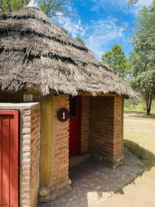 een bakstenen gebouw met een rieten dak en een rode deur bij Complejo Las Sierras in Nono