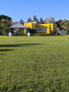 Um grande campo gramado com uma casa amarela ao fundo. em Cabañas La Soñada em Chajarí