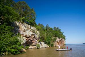 two people on a boat in the water next to a cliff at The Riverside Cottage in Dardanelle