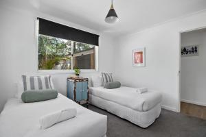 two beds in a room with white walls and a window at Bluegum Beach Stay in Narrawallee