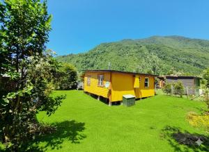 Uma casa amarela em um gramado com uma montanha ao fundo. em Cabaña Alto Puelo em Puelo