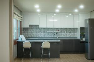 een keuken met witte kasten en 2 barkrukken bij welcalm village in Naemulch'i-ri