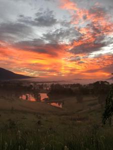 Cob Cabin - Sacred Earth Farm في Pumpenbill: غروب الشمس فوق حقل مع نهر في الأفق