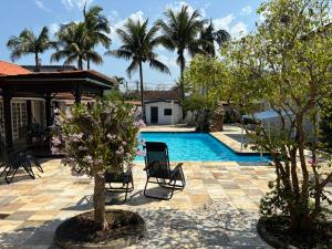 a swimming pool with two chairs and palm trees at Moreno Guest House com Piscina, churrasqueira Praia de Itaguaré e Riviera in Bertioga