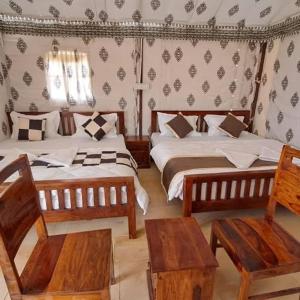 1 dormitorio con 2 camas y 2 sillas de madera en Desert camp Sam, en Sām 4 fotos más