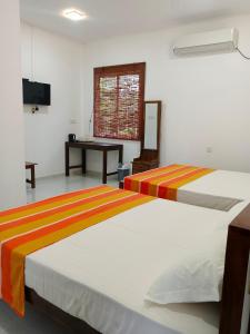 two beds in a room with a desk and a television at Didula Holiday Resort Anuradhapura in Anuradhapura