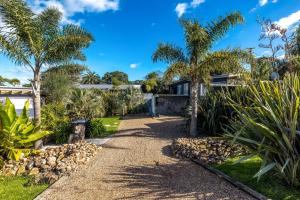 a pathway with palm trees in front of a house at Welcome Cottage - Stay Waiheke in Oneroa