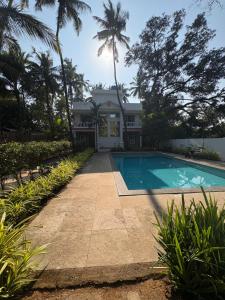 a house with a swimming pool and palm trees at Nature's Inn Luxury Villa Morjim Goa in Pernem