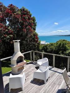a patio with two white chairs and a fireplace at Black Cottage - Stay Waiheke in Waiheke Island