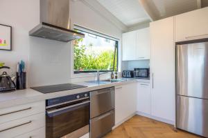Una cocina con gabinetes blancos y un refrigerador de acero inoxidable. en Black Cottage - Stay Waiheke, en Waiheke Island