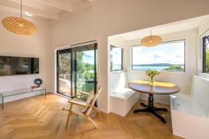 Una habitación con una mesa y sillas y ventanas. en Black Cottage - Stay Waiheke, en Waiheke Island