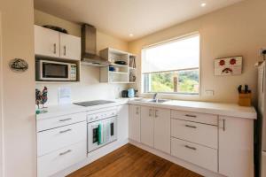 Una cocina con gabinetes blancos y una ventana. en Beachlovers Onetangi - Stay Waiheke, en Waiheke Island