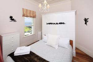 Crescent Villa - Stay Waiheke في Ostend: غرفة نوم مع سرير مع شراشف بيضاء وثريا +3 صور