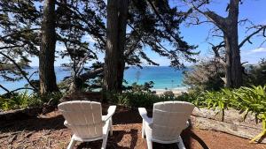 two white chairs sitting next to the beach at Viewpoint - Stay Waiheke in Onetangi