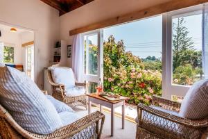 a living room with chairs and a table and a large window at Sunshine Cottage by the Sea - Stay Waiheke in Onetangi