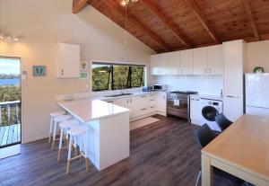 een keuken met witte kasten en een tafel en stoelen bij Church Bay Views - Stay Waiheke in Oneroa