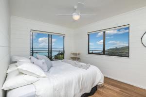 een witte slaapkamer met een groot bed en ramen bij Sunset Sanctuary- Stay Waiheke in Omiha +15 foto's
