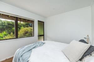 een witte slaapkamer met een bed en een raam bij Sunset Sanctuary- Stay Waiheke in Omiha