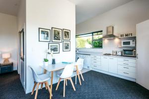 a kitchen with white cabinets and a table and chairs at Delamore Cove - Kauri - Stay Waiheke in Matiatia Bay +11 photos