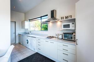 a kitchen with white cabinets and a washer and dryer at Delamore Cove - Kauri - Stay Waiheke in Matiatia Bay