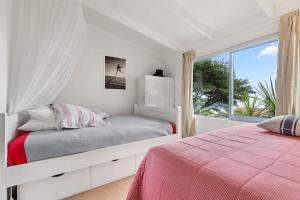 een witte slaapkamer met een bed en een raam bij Palm Views - Stay Waiheke in Palm Beach