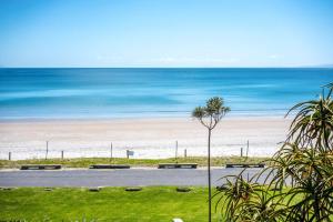 a beach with benches and the ocean in the background at The Sands - Villa 28 - Stay Waiheke in Onetangi
