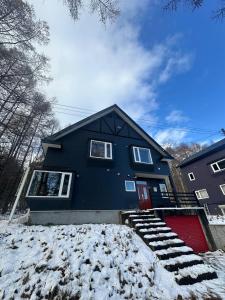 een blauw huis met een rode deur in de sneeuw bij Pine House in Rankoshi