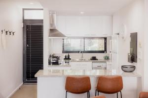 a white kitchen with a counter and some brown chairs at Heart of Hobart | CBD Apartment & Parking in Hobart