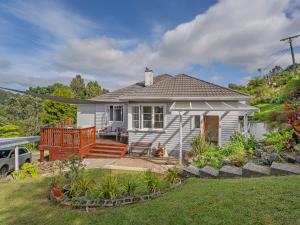 a small white house with a porch and a deck at Coro Harbour View - Coromandel Holiday Home in Coromandel Town