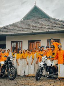 Private Pool Villa in Thodupuzha- Heliconia Inn في Thodupuzha: مجموعة من الأشخاص يرتدون قمصانًا برتقالية يقفون بجوار دراجات نارية