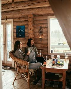 two women sitting on a chair in a room with a table at Romantic stay at loghouse VäikeTeeMaja in Üksnurme