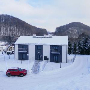 a red car parked in front of a building in the snow at Apartment Roku 2024 - JELEŃ & NATURA in Kudowa-Zdrój