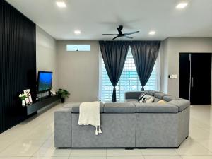 ein Wohnzimmer mit grauem Sofa und einem Fernseher in der Unterkunft 4BR Cozy Villa for 16 Pax Quiet Area & Spacious in Simpang Ampat