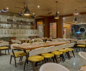 a dining room with a long table and yellow chairs at Hotel Zorba Inn in Kolhapur +36 photos