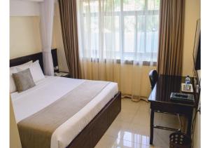 Un dormitorio con una cama y un escritorio y una ventana. en The Pinecone Hotel Kisumu, en Kisumu
