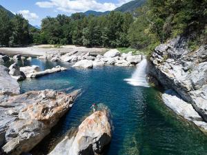 a person swimming in a river with a waterfall at Schöne Gartenwohnung am Strand von Tegna Centovalli in Tegna +5 photos