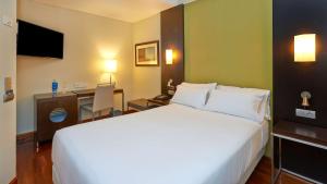 a hotel room with a large white bed and a desk at NH Sport in Zaragoza +22 photos