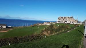a golf course with a house and the ocean at Poseidon's in Lossiemouth