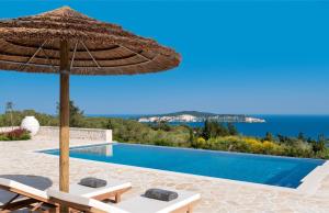 - une piscine avec un parasol et des chaises en paille dans l'établissement Villa Moundela, à Katsimátika