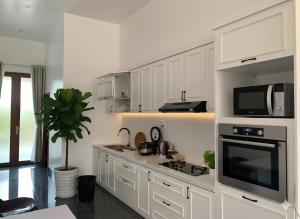 a kitchen with white cabinets and a stove and microwave at Pin's House - Nhà Nghỉ Dưỡng Nguyên Căn 4 phòng ngủ 4 WC Đầy Đủ Tiện Nghi in Bảo Lộc