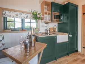 a kitchen with green cabinets and a wooden table at Poppie's Shepherd Hut - Uk50227 in Redmile