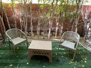 two chairs and a table in a yard with trees at Cozy Mini Villa with a backyard in 6th Of October
