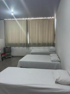two beds in a room with a window with white sheets at Aqui Hotel in Patos de Minas
